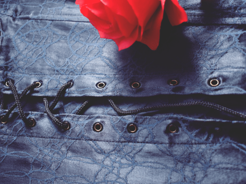 close up view of navy blue corset lacing with a red rose on top.