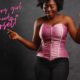 a woman wears a pink corset over black jeans. She is smiling and looks like she is dancing. text reads "every girl needs a corset".