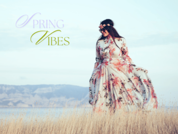 a woman in a rose print dress is walking in a grass field with the coastline in the background. She has a garland of roses around her head. Text reads "spring vibes".